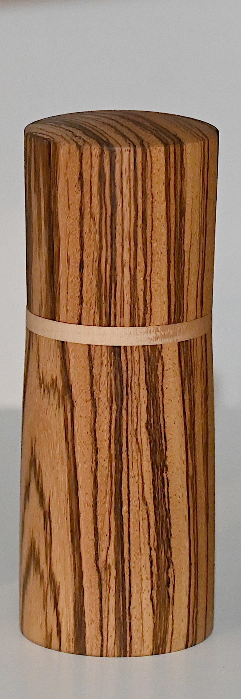 May include: A cylindrical wooden box with a natural wood grain pattern and a light brown band around the middle.
