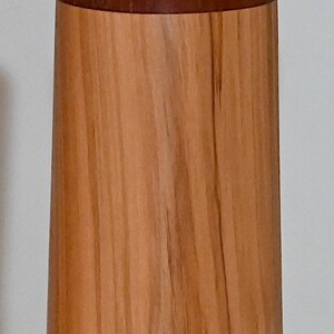 May include: A wooden pepper mill with a brown wood grain and a thin brown band around the middle.
