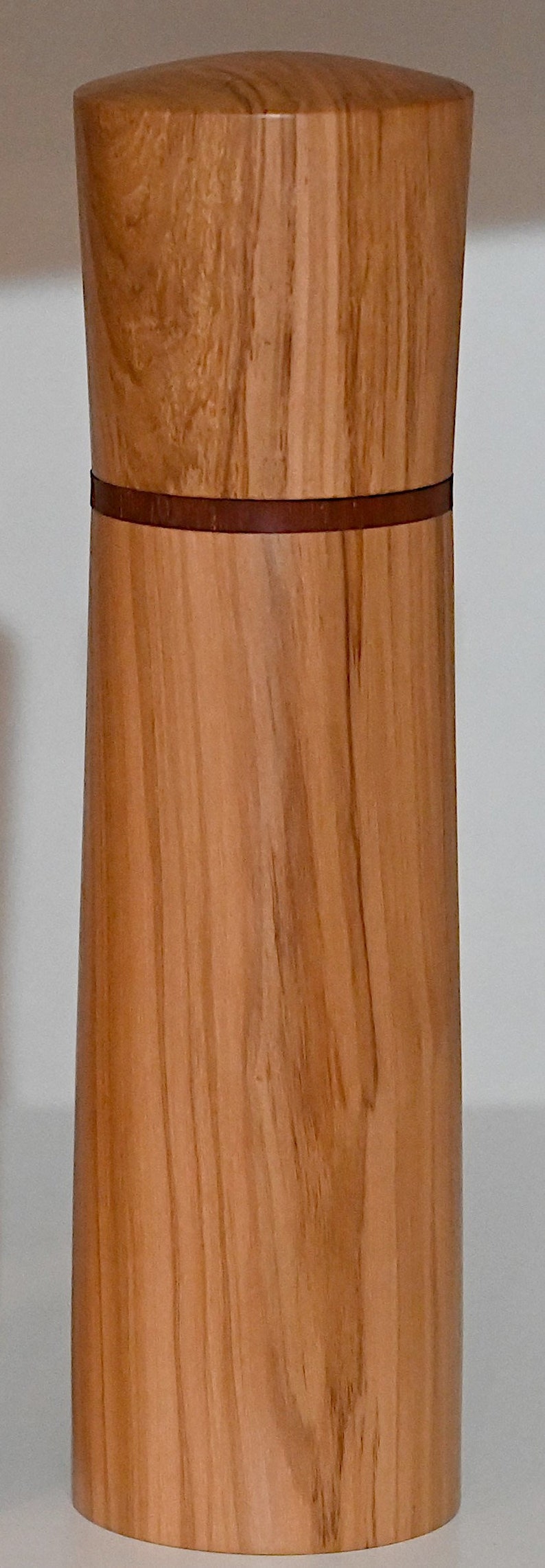 May include: A wooden pepper mill with a brown wood grain and a thin brown band around the middle.
