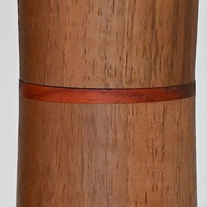 May include: A cylindrical wooden container with a red band around the middle. The container is made of a light brown wood with a natural grain pattern.