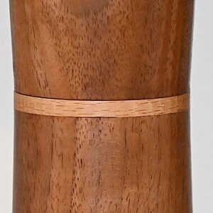 May include: A cylindrical wooden container with a light brown wood grain and a thin band of lighter wood around the middle.