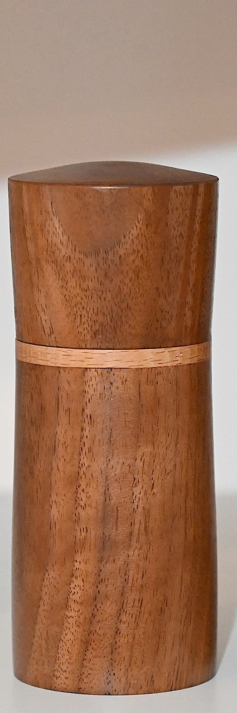 May include: A cylindrical wooden container with a light brown wood grain and a thin band of lighter wood around the middle.