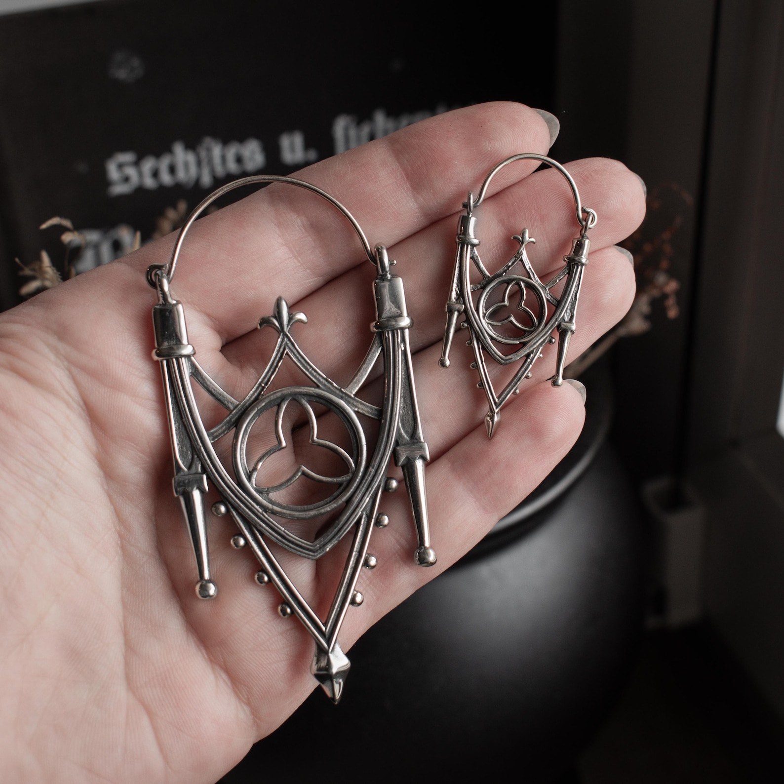 Silver gothic arch earrings with medieval cathedral detailing shown in hand for scale