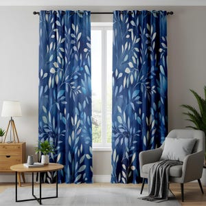 Op de afbeelding: Een paar blauwe gordijnen met een wit bladmotief. De gordijnen hangen aan een raam in een woonkamer.