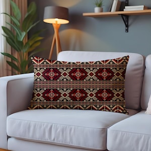 May include: Rectangular decorative pillow with a geometric pattern in red, black, and beige. The pillow features a repeating design of diamonds, stars, and other shapes. The pillow is placed on a white sofa.