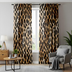 May include: A pair of brown and black leopard print curtains hang in a living room window. The curtains are made of a soft, flowing fabric and have a subtle sheen. The curtains are hung on a metal rod and are pulled back to reveal a window with a view of a garden.