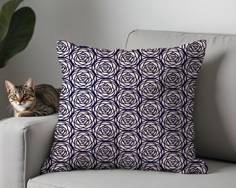 May include: Square throw pillow with a repeating pattern of navy blue rose outlines on a cream background. The pillow is on a white sofa. A tabby cat is visible on the left side of the image.