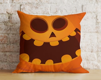 May include: Orange Halloween-themed decorative pillow featuring a cartoon jack-o'-lantern face. The pillow has a smiling face with large eyes and a wide mouth. The background is a light brick wall and a wooden surface.