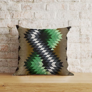 Puede incluir: Una almohada decorativa con un patrón geométrico en tonos de verde, negro, blanco y marrón. La almohada tiene una textura tejida y un diseño contemporáneo.