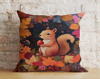 Könnte beinhalten: Ein Kissen mit einem bunten Herbstlaubmuster, auf dem ein Eichhörnchen eine rote Beere hält. Das Eichhörnchen ist von Blättern in Orange-, Rot-, Gelb- und Brauntönen umgeben.