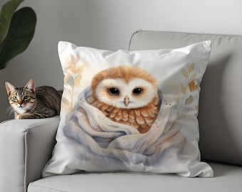 May include: A square cushion with a watercolour illustration of a brown and white owl nestled in a blue blanket. The owl has large, dark eyes and is set against a white backdrop. A tabby cat is visible on the left side of the image.
