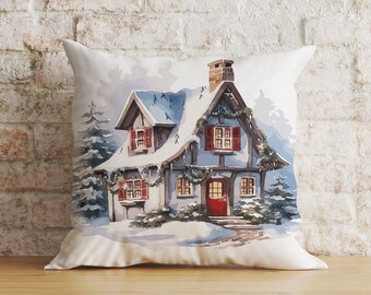 May include: A white throw pillow with a watercolor illustration of a snow-covered cottage with red shutters and a red door. The cottage is surrounded by trees and snow.