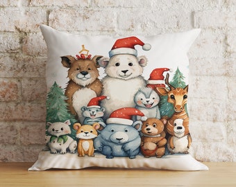 Peut inclure: Un oreiller blanc avec une scène de Noël festive mettant en scène un ours polaire, un cerf, un chien et d'autres créatures des bois portant des bonnets de Père Noël. L'oreiller est décoré d'un sapin vert et de baies rouges.