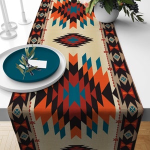 May include: A beige table runner with a geometric pattern in shades of orange, blue, black, and white. The pattern features a repeating design of triangles and diamonds.