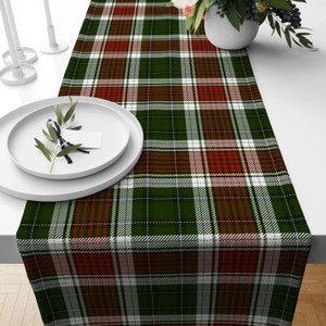 May include: A green, red, and white plaid table runner with a white background. The runner is made of a woven fabric and has a subtle sheen.