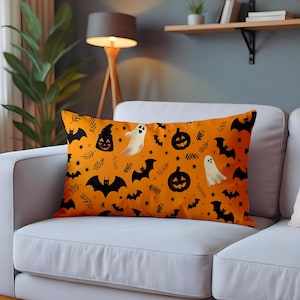 May include: Orange rectangular pillow with a Halloween-themed pattern. The design includes black bats, ghosts, jack-o'-lanterns, stars, and sprigs. The pillow is resting on a white sofa.