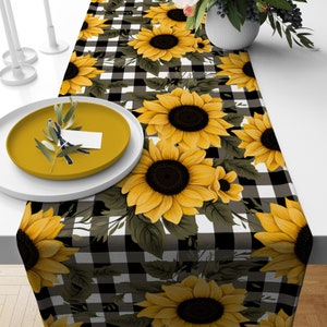 May include: Black and white checkered table runner with a sunflower pattern. The runner features yellow sunflowers with brown centers and green leaves.