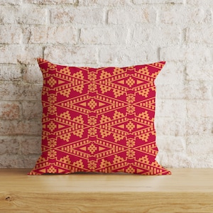 Puede incluir: Una almohada roja con un patrón geométrico en naranja. El patrón está formado por diamantes, cuadrados y otras formas.
