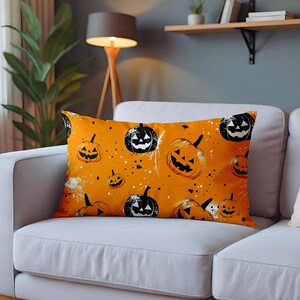 Może przedstawiać: Pomarańczowa, prostokątna poduszka dekoracyjna z wzorem dyni na Halloween. Poduszka przedstawia różne rozmiary lampionów z dyni w kolorze czarnym i pomarańczowym, z białymi plamami. Poduszka leży na białej sofie.