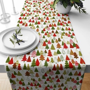 Könnte beinhalten: Ein weißer Tischläufer mit einem sich wiederholenden Muster aus bunten Weihnachtsbäumen. Die Bäume sind rot, grün und gold mit weißen Akzenten.