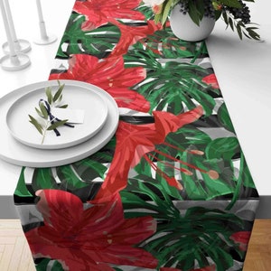 May include: A tropical table runner with a black and white striped background. The runner features large red flowers and green leaves.