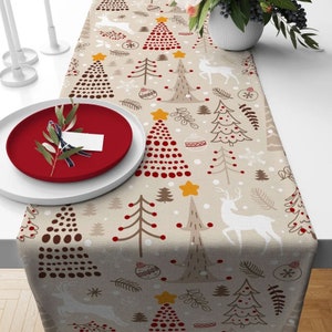 May include: A beige table runner with a Christmas tree design. The pattern features red, brown and white Christmas trees, snowflakes and reindeer. The runner is ideal for adding a festive touch to your Christmas table.