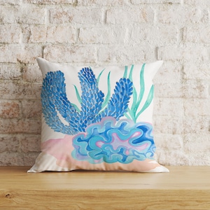 May include: A white pillow with a blue and pink watercolor design of coral and seaweed. The design is stylized and abstract.