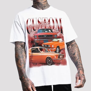 May include: White t-shirt with a graphic print of three orange and red vintage Ford Mustang cars. The text "Custom Here" is printed in red on the shirt.