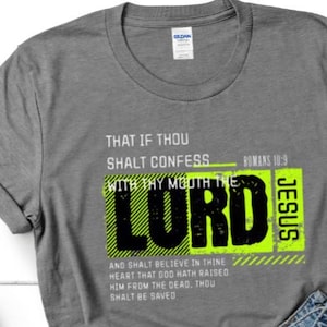 May include: A gray t-shirt with the text "THAT IF THOU SHALT CONFESS WITH THY MOUTH THE LORD JESUS" in black and neon green. The shirt also includes the Bible verse Romans 10:9.
