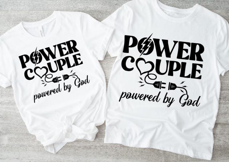 Op de afbeelding: Twee witte T-shirts met zwarte tekst en afbeeldingen. De tekst op beide shirts luidt "Power Couple powered by God". De afbeelding is een hart met een bliksem en een stekker en snoer.