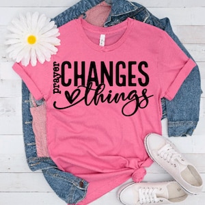 May include: Pink t-shirt with the text "prayer changes things" in black lettering with a small heart graphic.