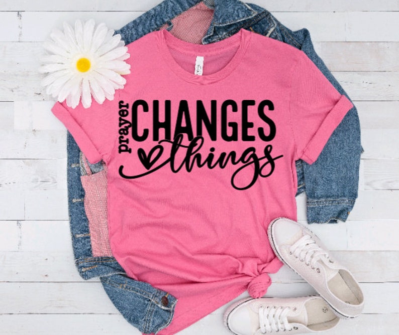 May include: Pink t-shirt with the text "prayer changes things" in black lettering with a small heart graphic.