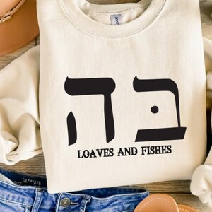May include: A cream-colored sweatshirt with black Hebrew lettering and the text "Loaves and Fishes".