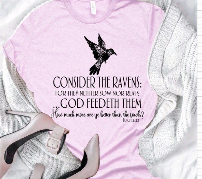 May include: A pink t-shirt with a black silhouette of a bird with floral details. The text "CONSIDER THE RAVENS: FOR THEY NEITHER SOW NOR REAP: ...GOD FEEDETH THEM How much more are ye better than the fowls? LUKE 12:23" is printed on the shirt.
