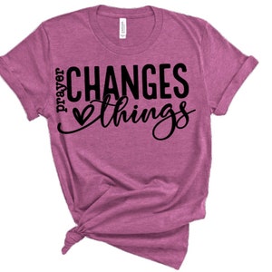 May include: A pink t-shirt with the text "prayer changes things" in black lettering with a heart symbol.