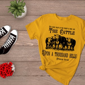 Puede incluir: Una camiseta amarilla con un gráfico negro de ganado y el texto "FOR EVERY BEAST OF THE FOREST IS MINE AND THE CATTLE UPON A THOUSAND HILLS PSALM 5010".