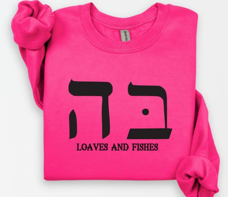 May include: A pink sweatshirt with black Hebrew lettering and the words "Loaves and Fishes" printed on the front.
