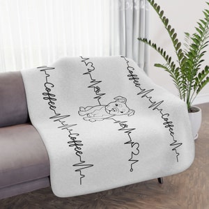Peut inclure: Jeté en polaire blanc avec une illustration noir et blanc d'un chien et le texte "Coffee" répété quatre fois avec un graphique de battement de cœur.