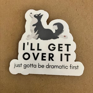 May include: A white sticker with a black and white cartoon dog lying down. The sticker says "I'll get over it, just gotta be dramatic first."