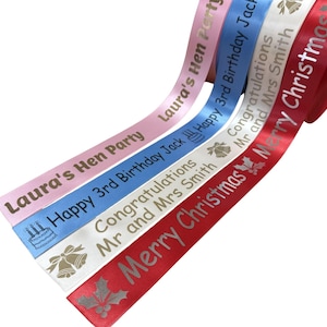 May include: A selection of colourful satin ribbons, each bearing a different celebratory message. The ribbons are printed with phrases such as "Laura's Hen Party", "Happy 3rd Birthday Jack", "Congratulations Mr and Mrs Smith", and "Merry Christmas."
