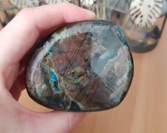 May include: A smooth, polished, dark gray and blue labradorite gemstone with iridescent flashes of color. The stone is heart-shaped and has a natural, organic shape.