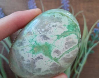 May include: A smooth, polished green and white agate stone with a swirling pattern. The stone is oval shaped and has a natural, organic look.