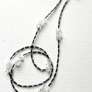 May include: Eyeglass chain with black beads and clear, irregular-shaped accents. The chain has silver-colored clasps to attach to glasses. The design is displayed on a white background.