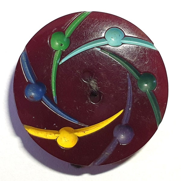 1 dark maroon celluloid button with swirled designs painted in yellow, blue, green and turquoise. 1940s. 2 sewing holes. 1" or 25.5mm. CB559