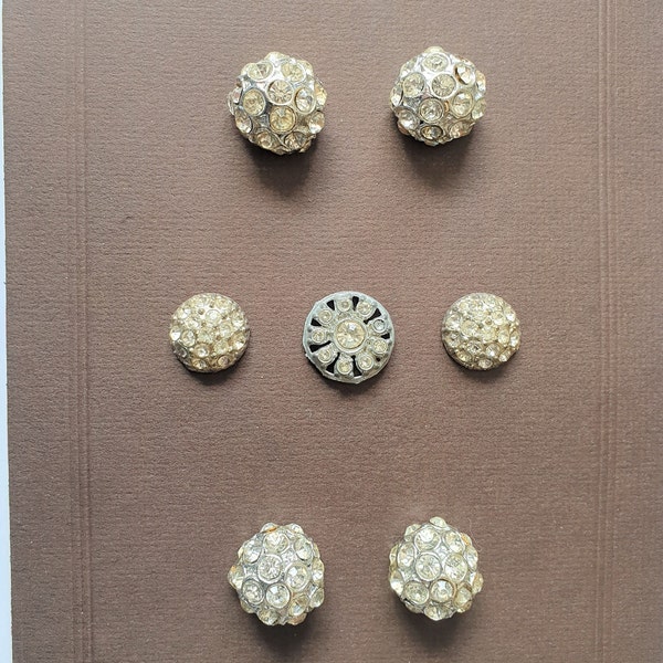 7 boutons en pâte blanche sur métal. 4 boules de 13/16", 2 bombées de 5/8" et 1 filigrane de 3/4". Tige en boucle en métal. Années 1950. Pâte 64