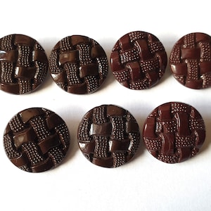 Puede incluir: Siete botones de plástico marrones con un patrón tejido. Los botones son redondos y tienen un diseño en relieve.