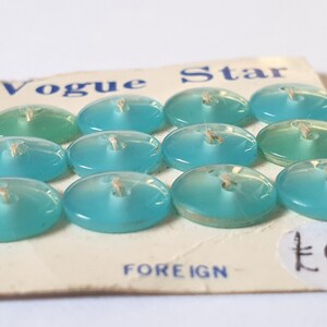 Een kaart met 12 kleine turquoise Vogue Star-knopjes. Celluloid. Ideaal voor poppen. Gelabeld buitenlands. 2 naaigaten. Jaren 1950.  5/16" of 8 mm. CB227