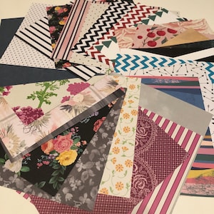 May include: A collection of patterned paper sheets in various designs and colors. The assortment includes floral, striped, polka dot, and geometric patterns. The color palette features pinks, blacks, whites, greens, and blues, creating a visually diverse and artistic arrangement.