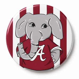 May include: A circular pinback button featuring a cartoon gray elephant wearing a maroon shirt with a white letter A on the front. The background consists of vertical maroon and white stripes. The elephant has large ears and a curved trunk.