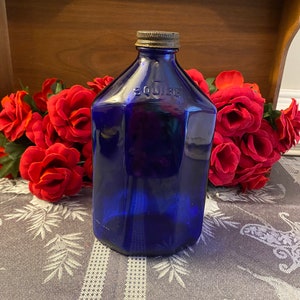 May include: A vintage cobalt blue glass bottle with a metal cap. The bottle has a unique octagonal shape and the word "SQUIRE" is embossed on the side. Red roses are in the background.